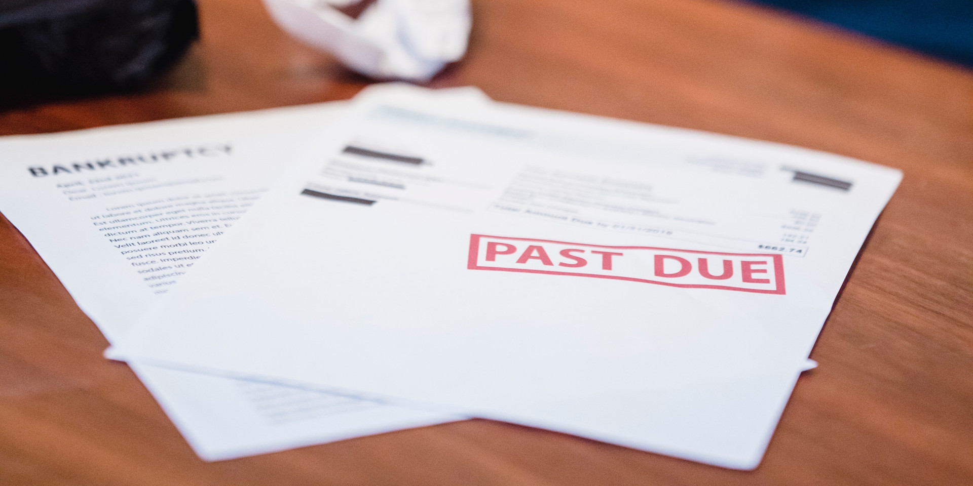 A past due bill and a form to file bankruptcy lie on a wooden desk.