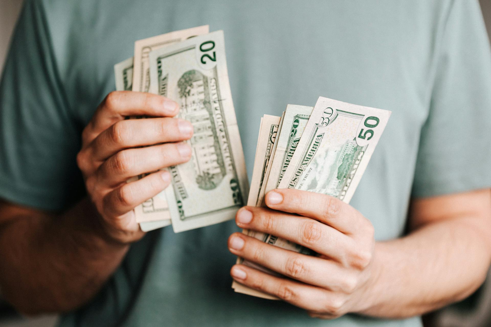 A man in a pistachio green t shirt counts dollar bills.
