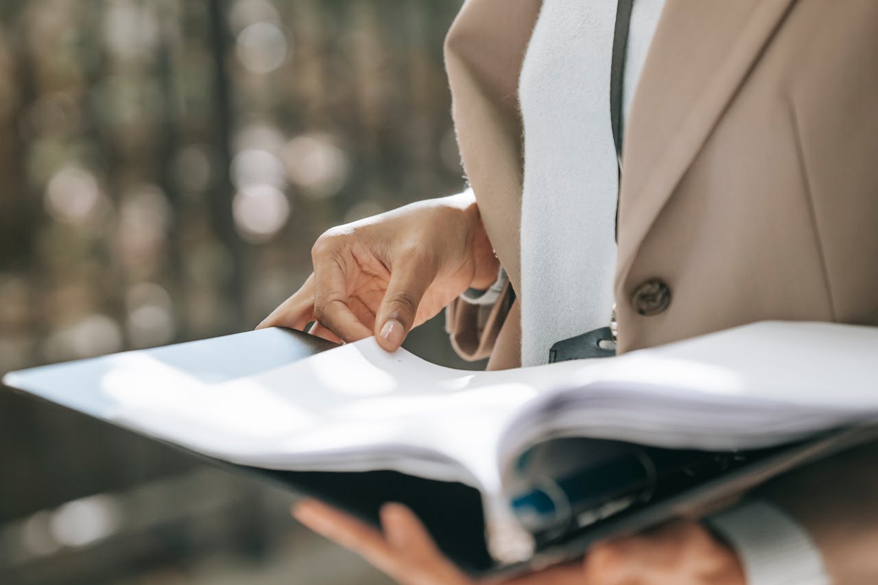 A close shot of a woman's torso and hands. She holds an open binder with documents in one hand and is holding a page with her other hand.