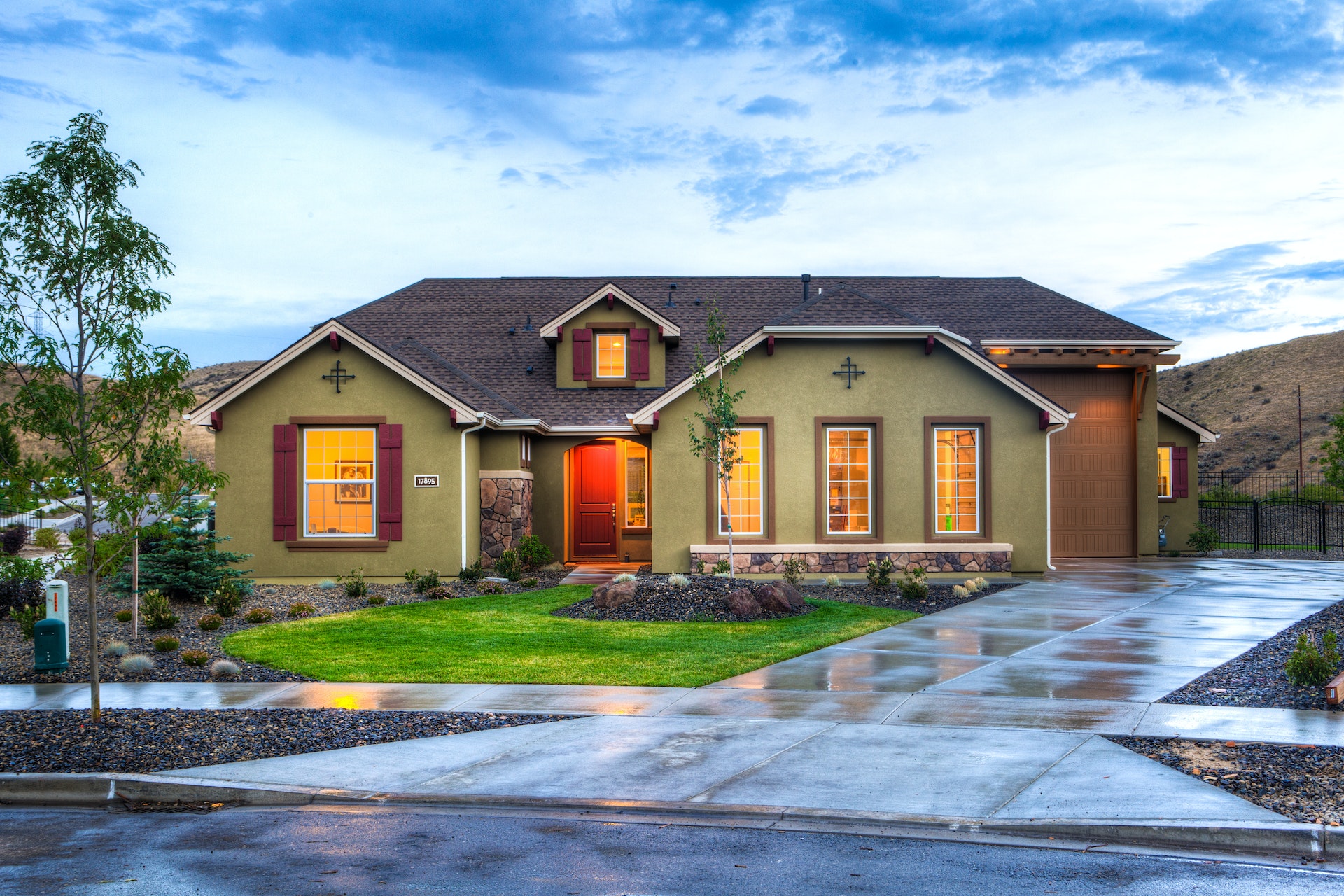 A photo of a single story home against a cloudy blue sky. The driveway and other pavement are wet.